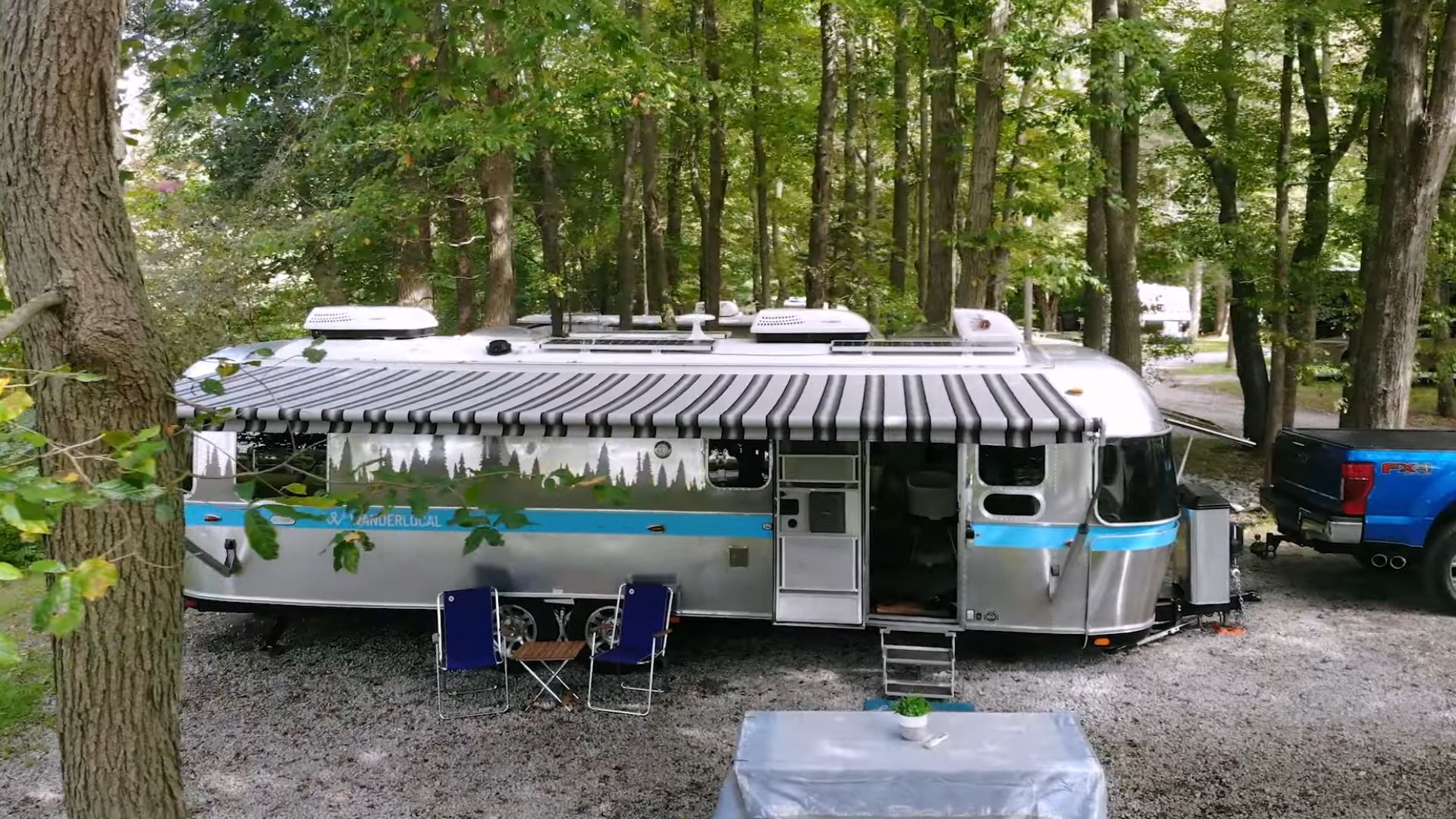 exterior of the Airstream with the awning, surrounded by greenery, blue decor lines on the Airstream