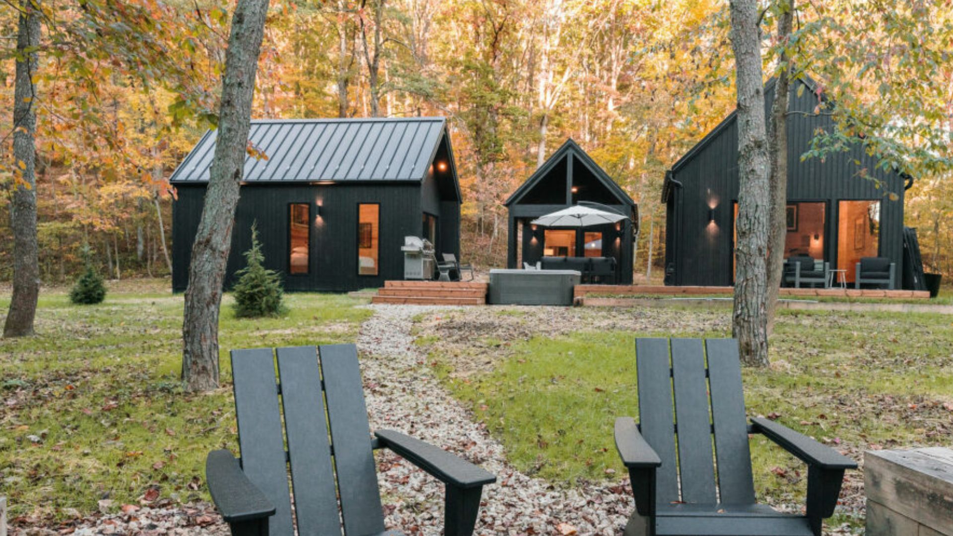 aerial view of a modern black cabin villa pine complex with four buildings connected by wooden decks, set in a wooded area with a hot tub and outdoor seating