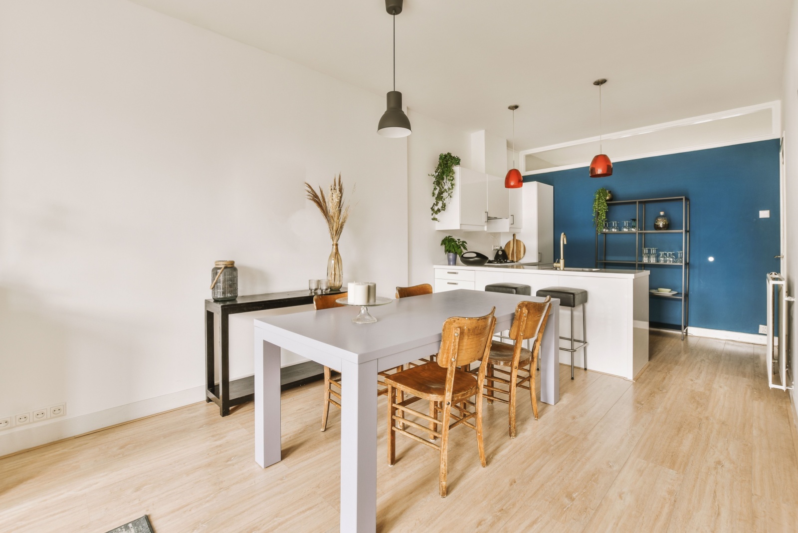 kitchen and dining room with white walls and one blue wall, light gray dining table and wooden chairs, white cabinets and a black shelf