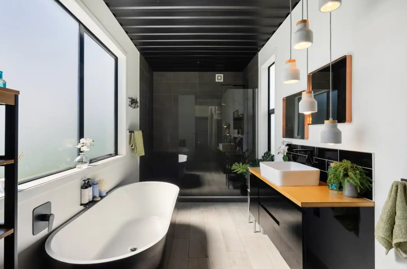 bathroom with a white bathtub, glass shower, black tiles in the shower, black cabinet with a wooden countertop, big window