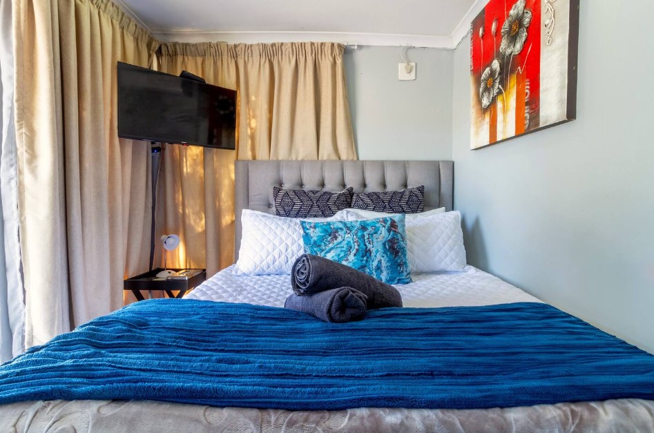 bedroom with a bed, black bedside table, flower artwork on the wall, flat-screen tv in the corner of the room