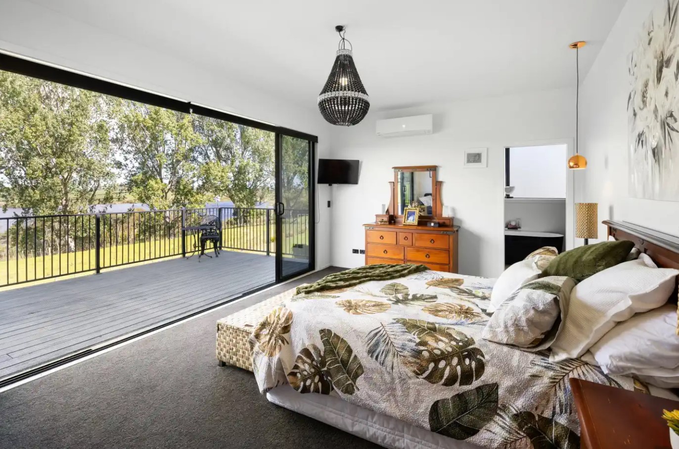 bedroom with a comfy bed and glass doors and a view opposite the bed, chandelier, low hanging lamp and a lamp on the bedside table, brown wooden cabinet with a mirror above