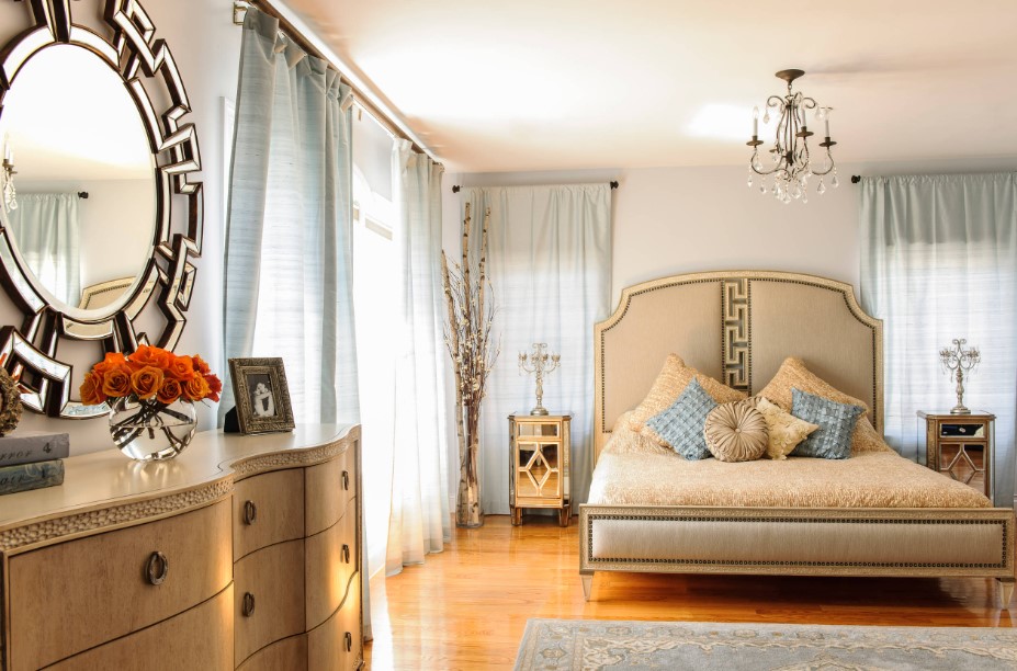 bedroom with a huge bed, brown cabinet and large windows with light blue curtains