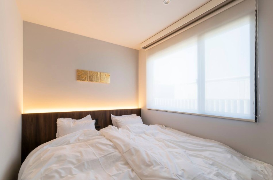 bedroom with white bed sheets, large window and white walls