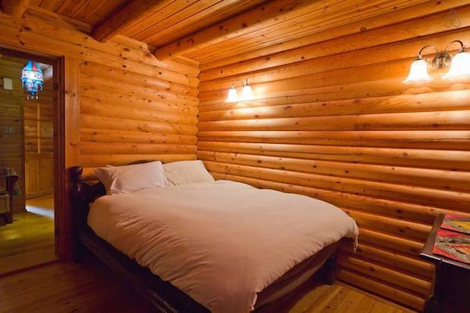 bedroom with a bed, wooden walls and warm lightning from the lamps on the wall