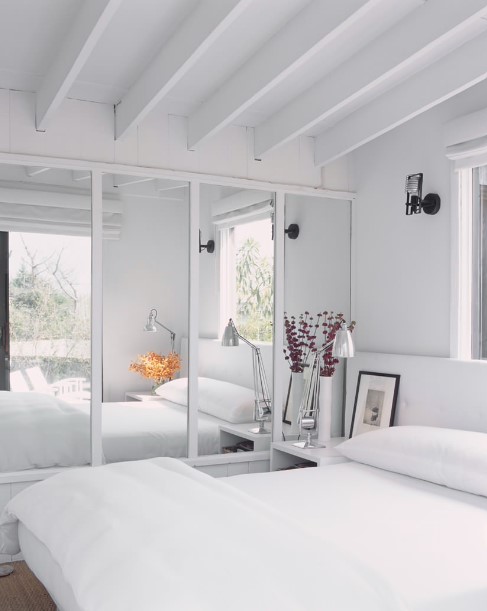 big mirror inside the bedroom with white walls, big bed and white bedside tables