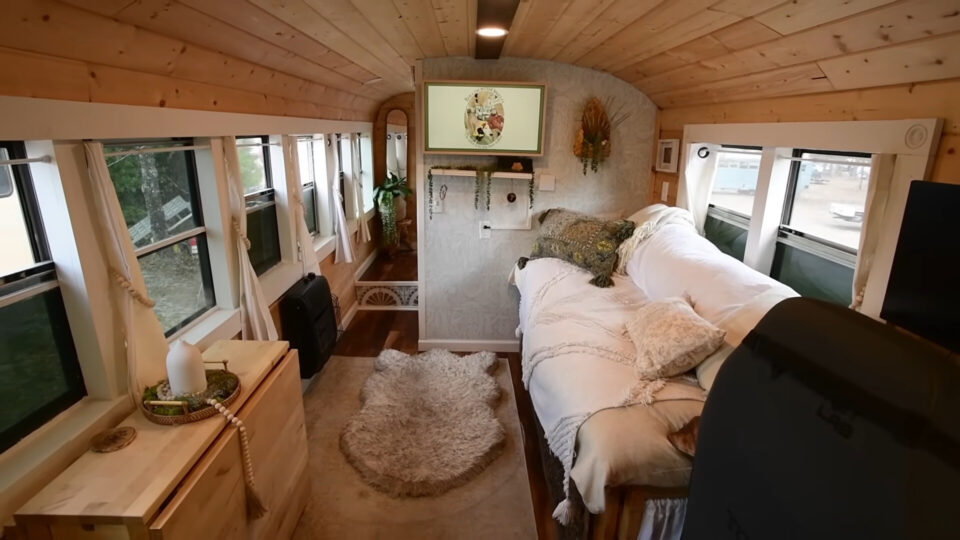 interior of a converted school bus home with a comfy couch, soft rug, wooden cabinet and a tv