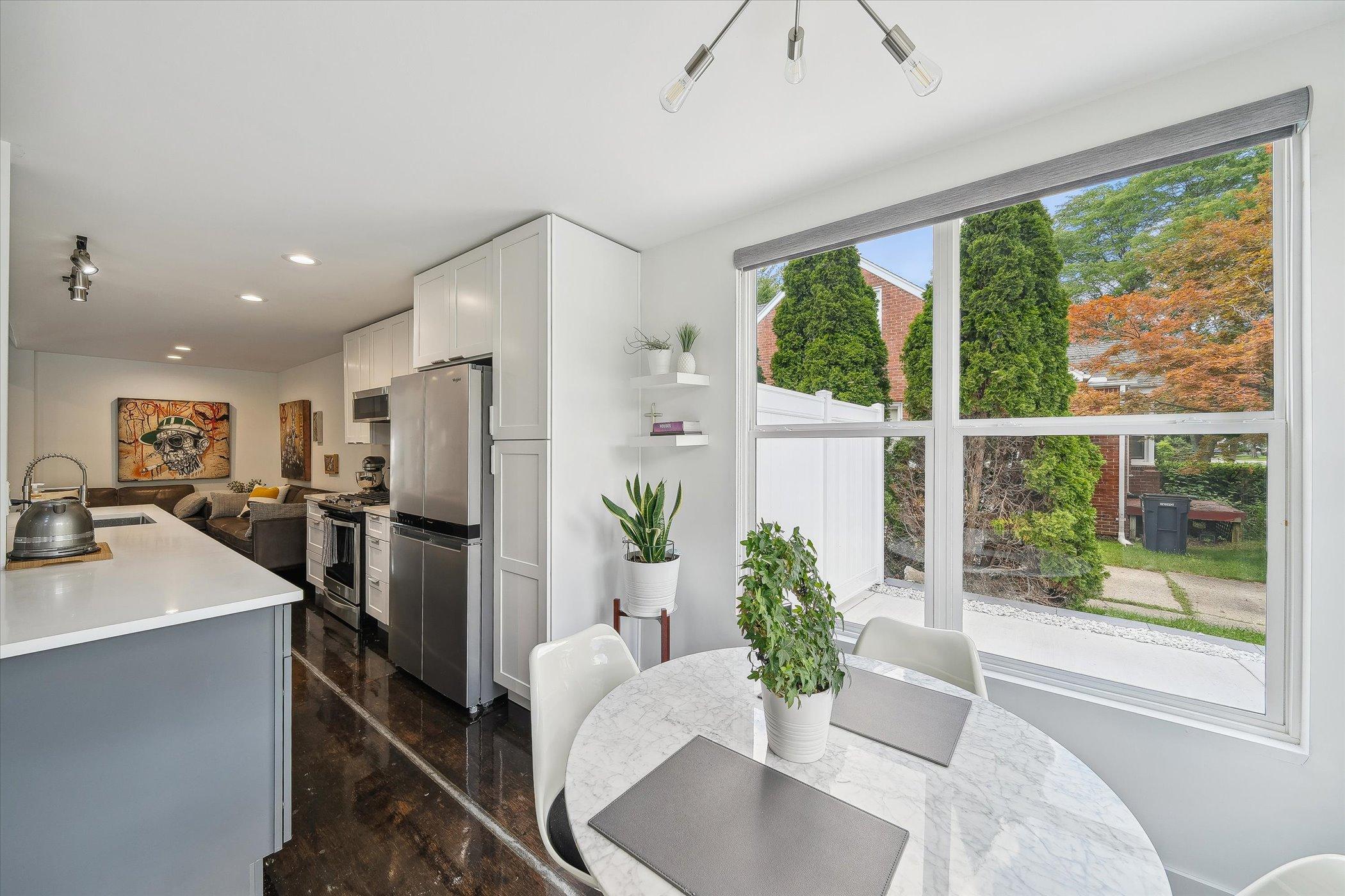 dining area with a round, white table with white chairs surrounded by windows and a kitchen with white cabinets in the background