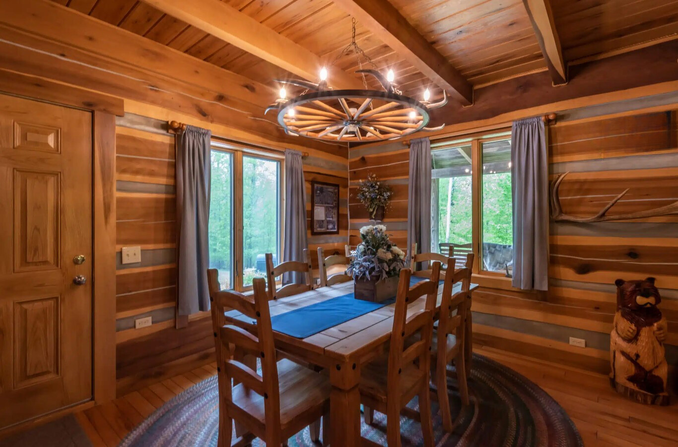 dining room with wooden walls, wooden dining table surrounded by wooden chairs and two big windows