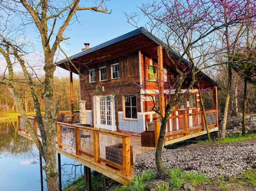 exterior of a cabin with a wraparound deck near the lake