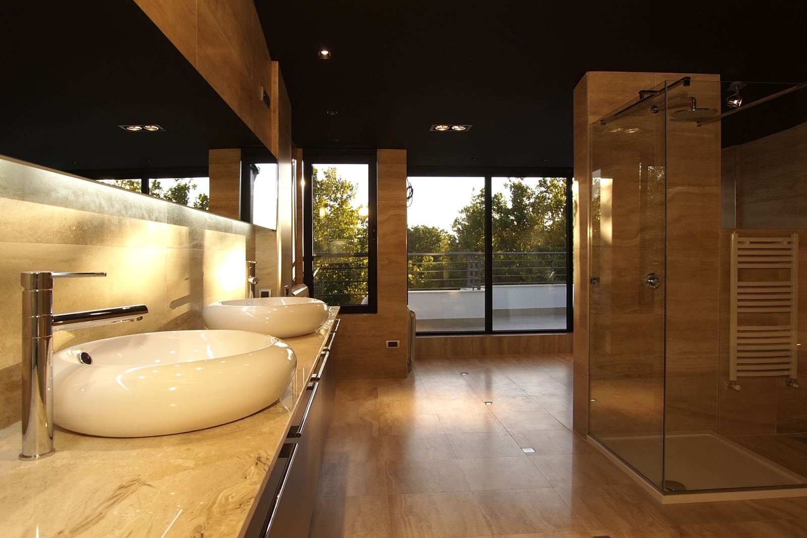 bathroom with warm, dim, mood lightning and round white sinks and a glass shower