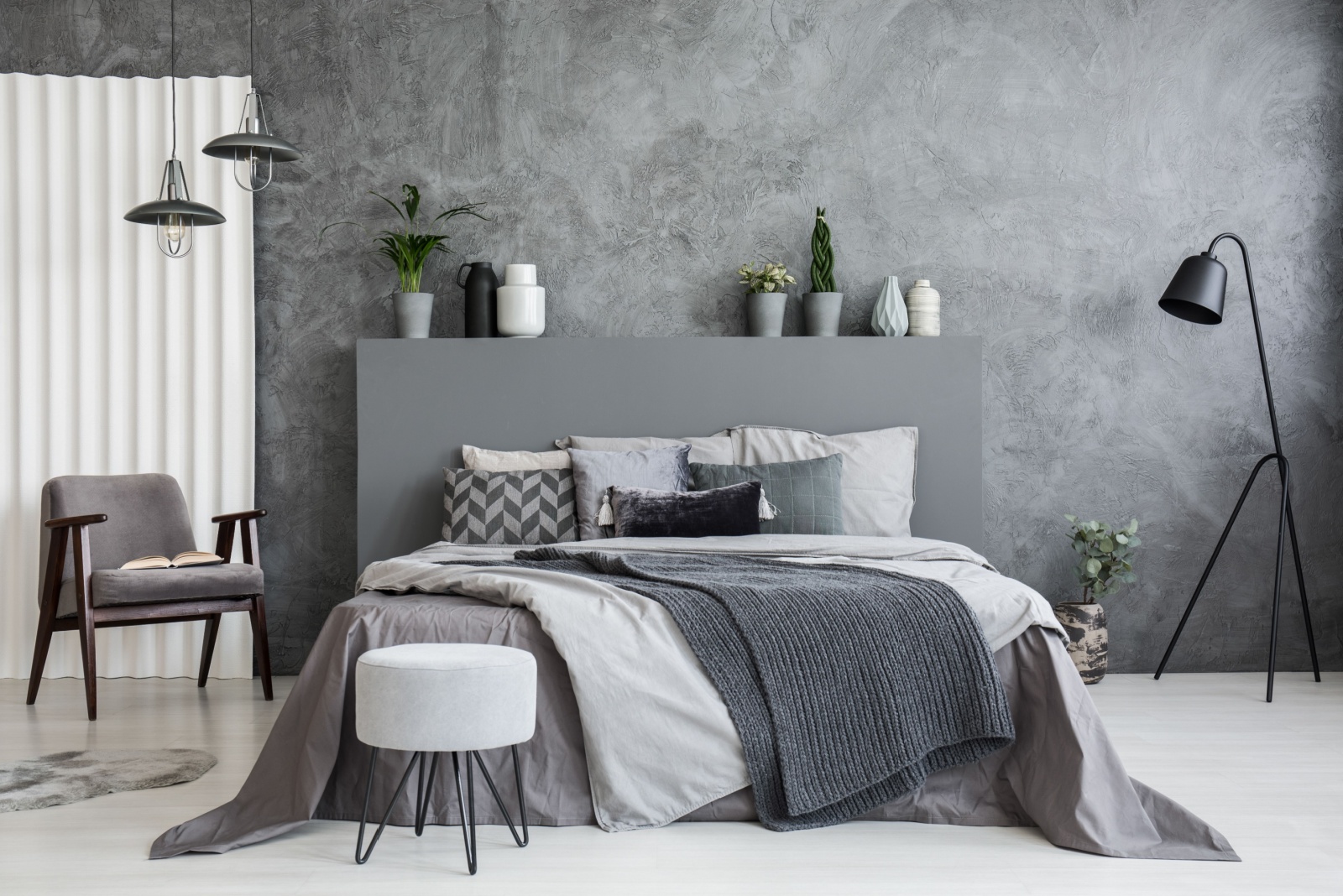 bedroom with a bed with a gray bed frame, gray wall, gray chair in the corner and a black lamp