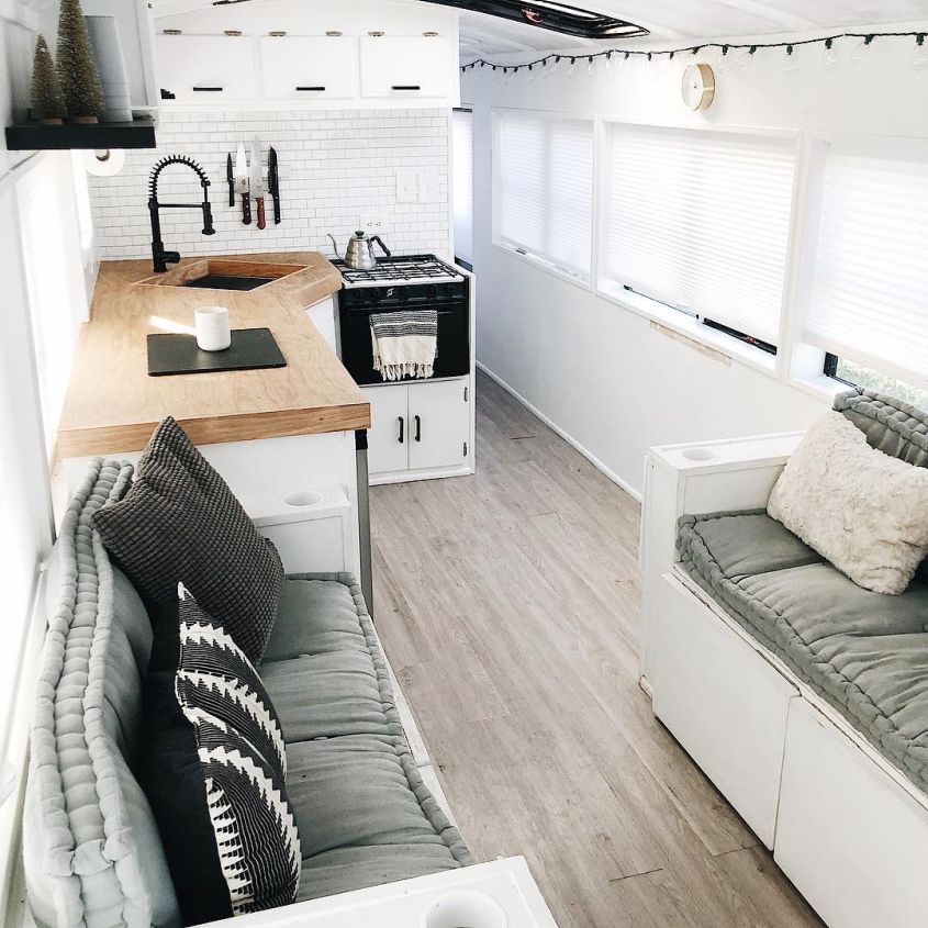 interior of a converted school bus with white couches opposite each other, wooden countertop