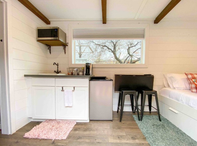 kitchen with white cabinets, microwave above, foldable black dining table with black stools and a window above