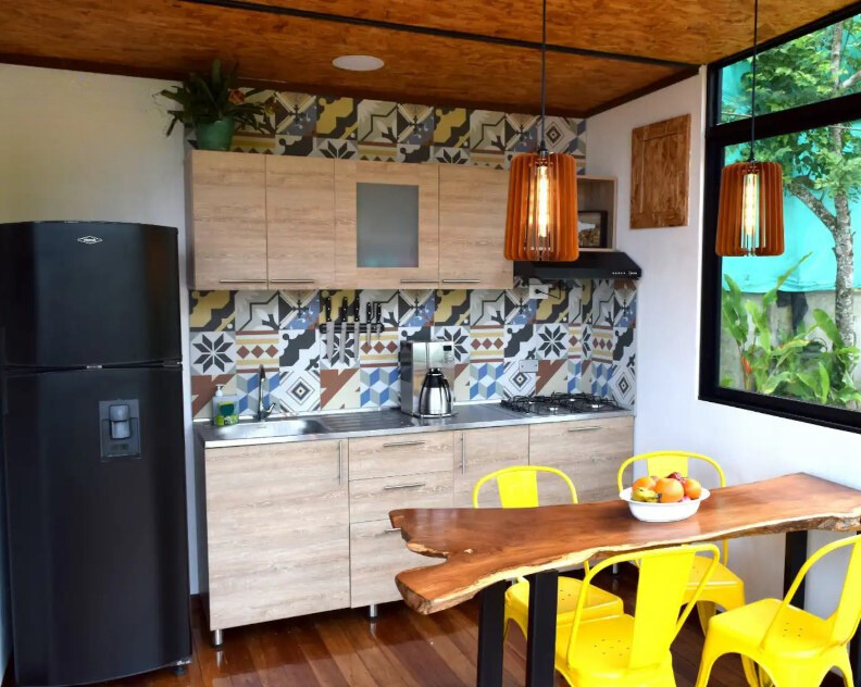 kitchen with colorful tiles between light brown cabinets, vivid yellow chairs and a unique brown dining table