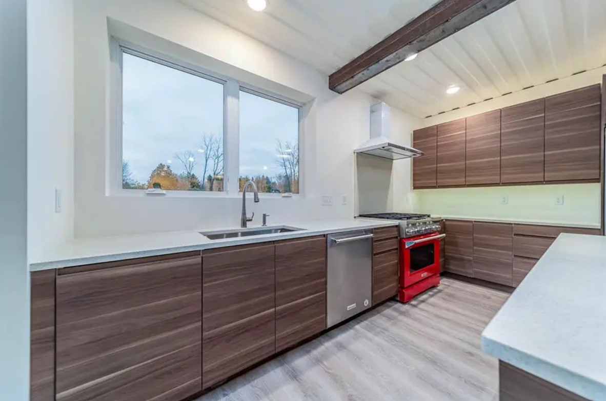 kitchen with brown cabinets, windows above the white countertop and a red oven