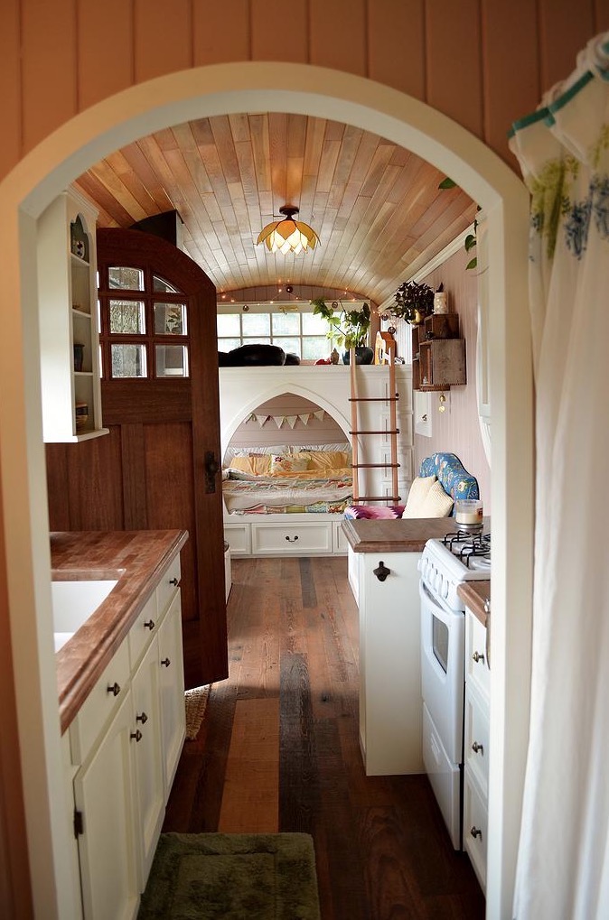 interior of a converted school bus with arched frames, a white bed, wooden doors