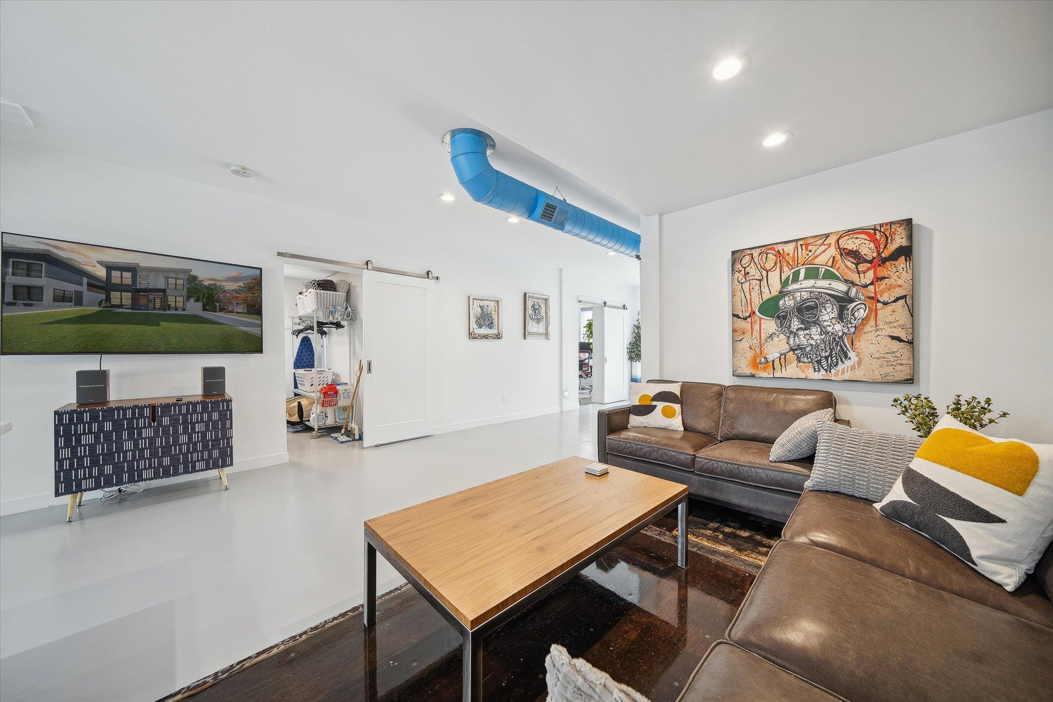 living area with a brown couch, table with a wooden top, artwork above the couch, flat screen tv