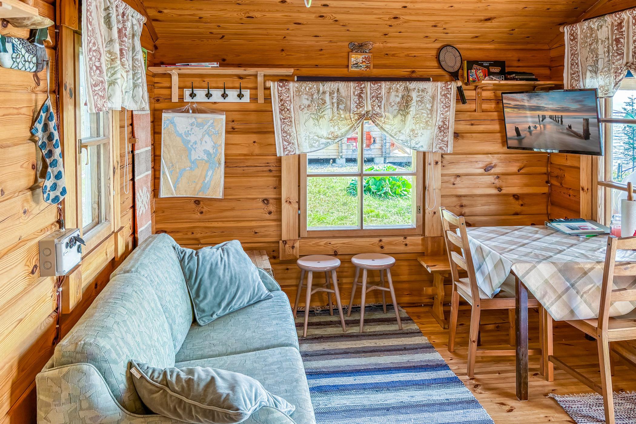 living room with a blue couch, flat screen tv, dining table, mini curtains above the windows