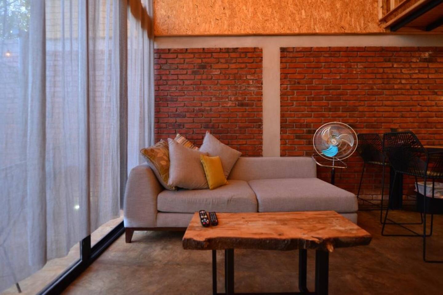 living room with a brick wall, concrete floor, sheer curtains, gray couch and a wooden table