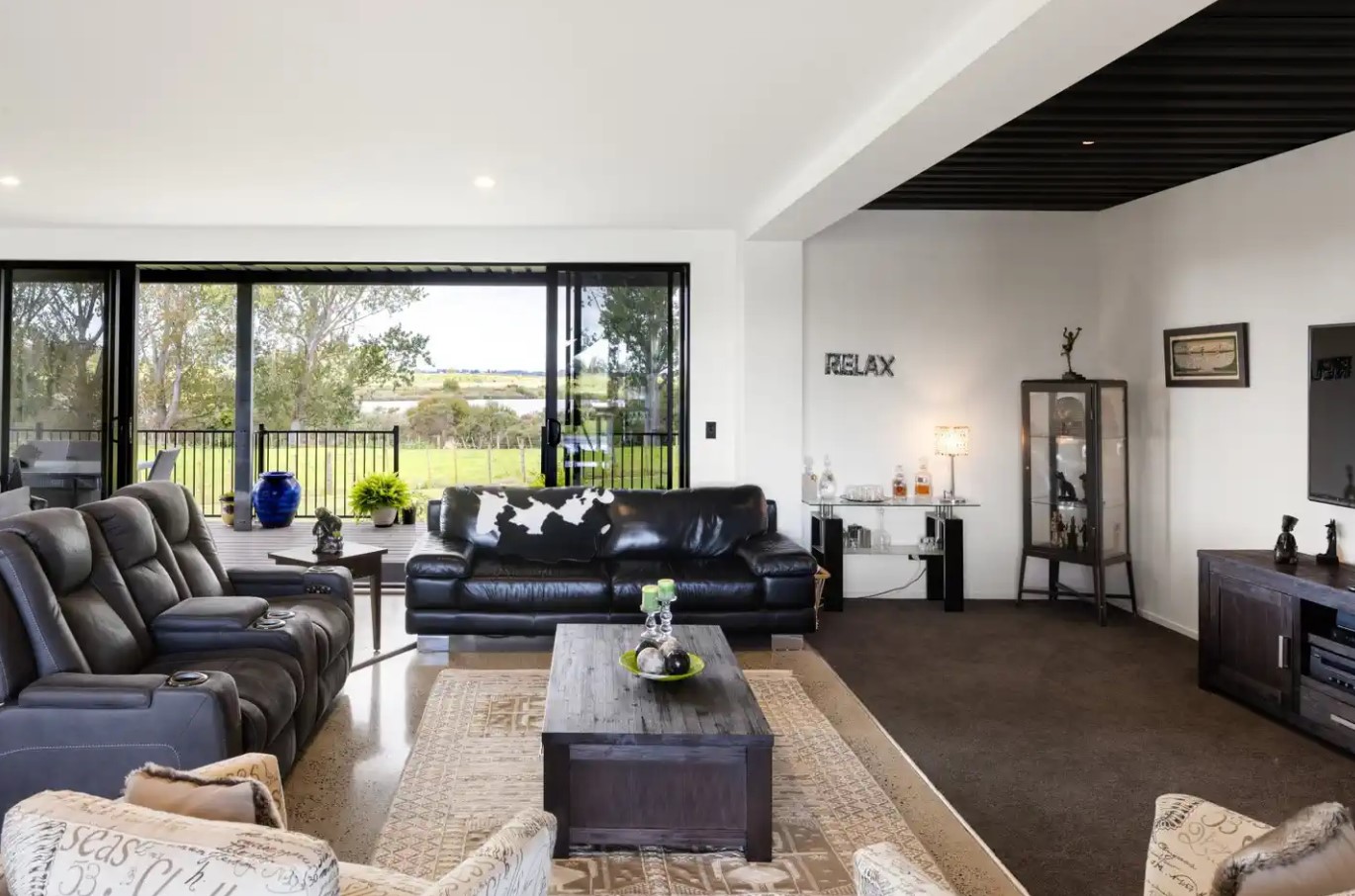 living room with black, leather couches, wooden table, a beige carpet under the table, flat-screen tv opposite the couch, glass doors