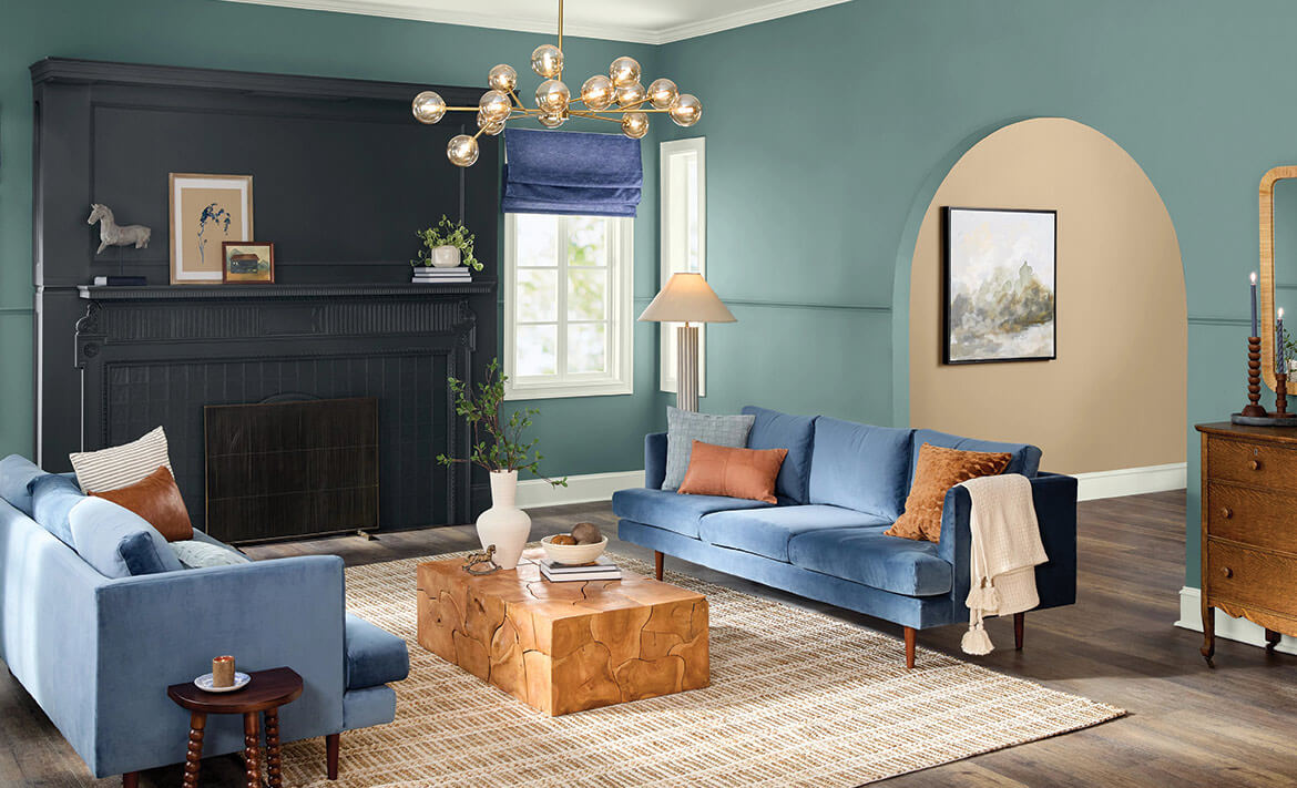 living room with a mapped blue wall, two blue couches, brown table in the middle, unique chandelier