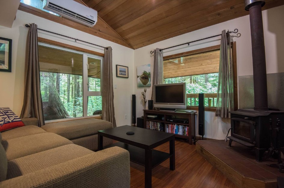 living room with a beige couch, two big windows, black table, fireplace, tv and a cabinet