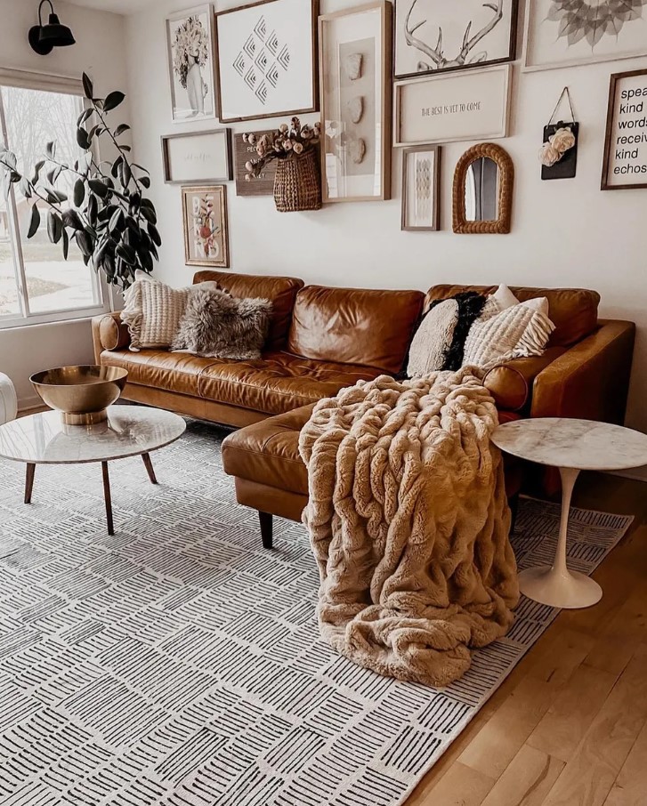 living room with an l-shaped leather brown couch, gray carpet, round tables, gallery wall