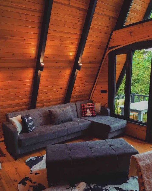 living room with a gray couch, wooden walls, warm light, floor to ceiling windows