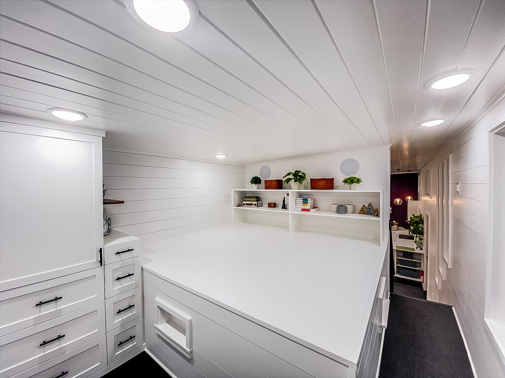 loft bedroom with a bed surrounded by storage drawers and open shelves, white walls