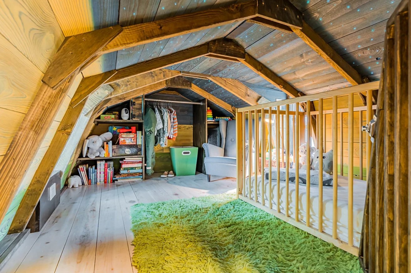 loft area with wooden walls, green fluffy carpet, a lot of books and clothes and plushies on one wall and one gray chair