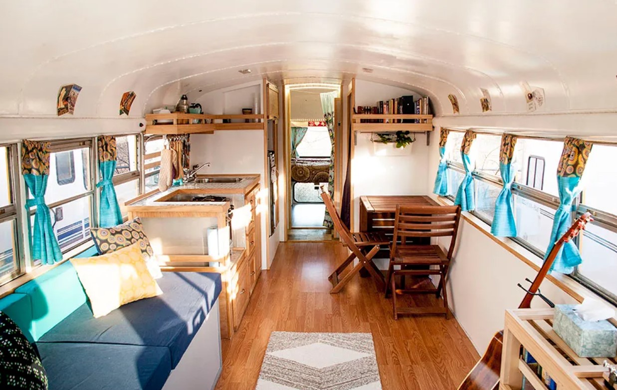 interior of a converted school bus with a wooden dining table and wooden chairs, blue cushioned built in couch