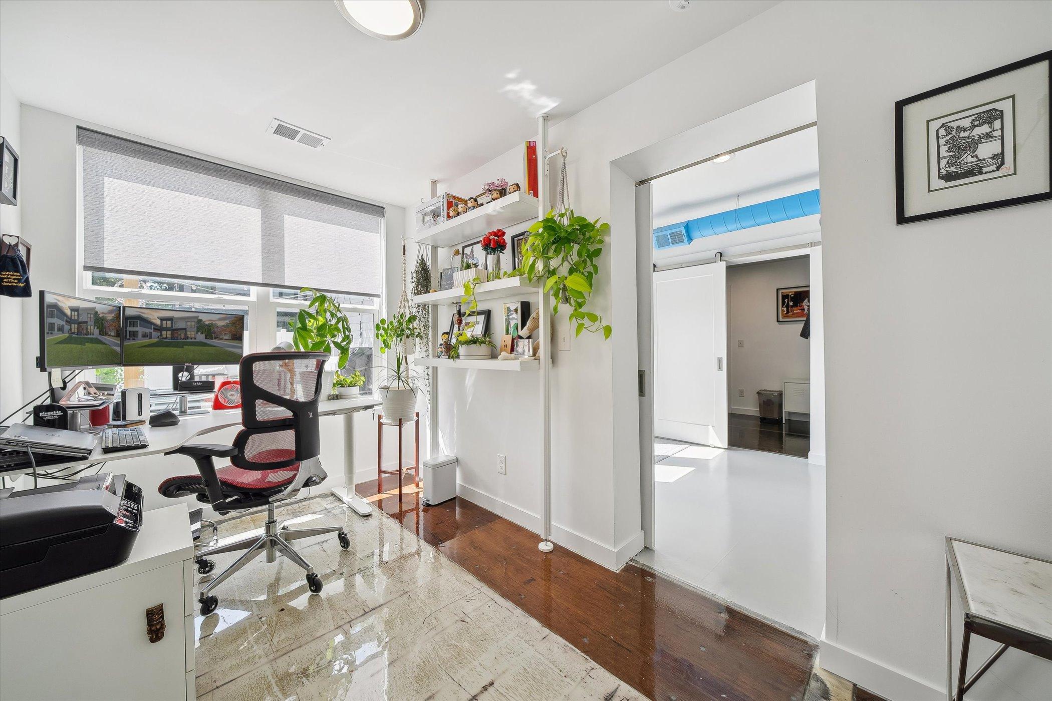 office room with a white desk, white walls and white shelves, computers on top of the desk and a cool chair