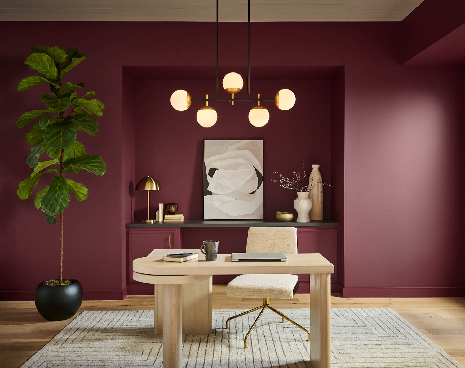 office room with a ruby rumors red wall, beige table accompanied by a chair, wonderful chandelier and a big plant