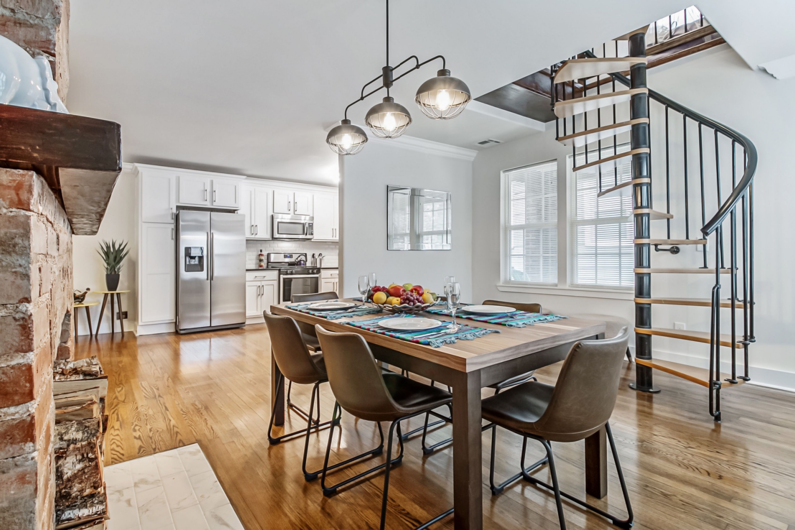 dining room with a dining table and brown chairs and a lamp above and a kitchen in the background