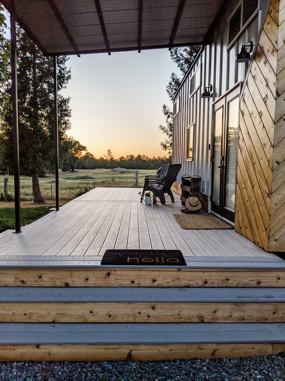 porch of a tiny home with two black chairs during a sunset