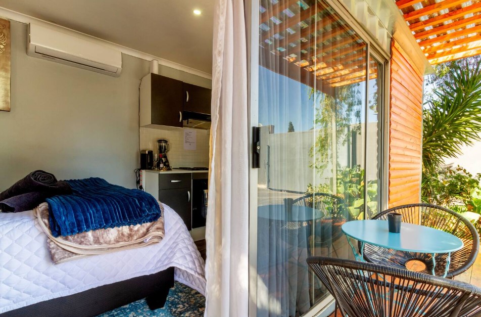 porch of a container with a round table accompanied by two chairs, with glass doors and a bedroom in the background