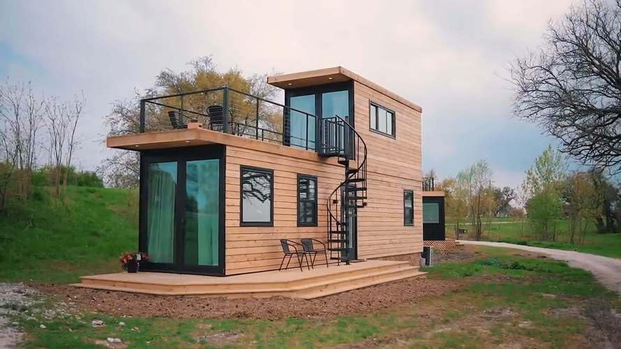 exterior of a container home with wooden walls, glass doors, spiral staircase with a terrace on the roof