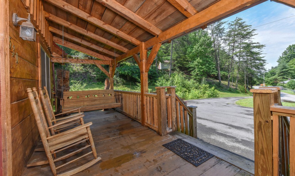 covered wooden deck of a cabin with a swing and chairs