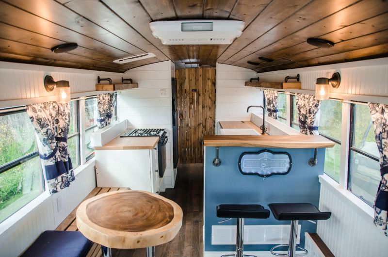 interior of a converted school bus with a mini kitchen with wooden countertops, a mini bar with two black bar stools