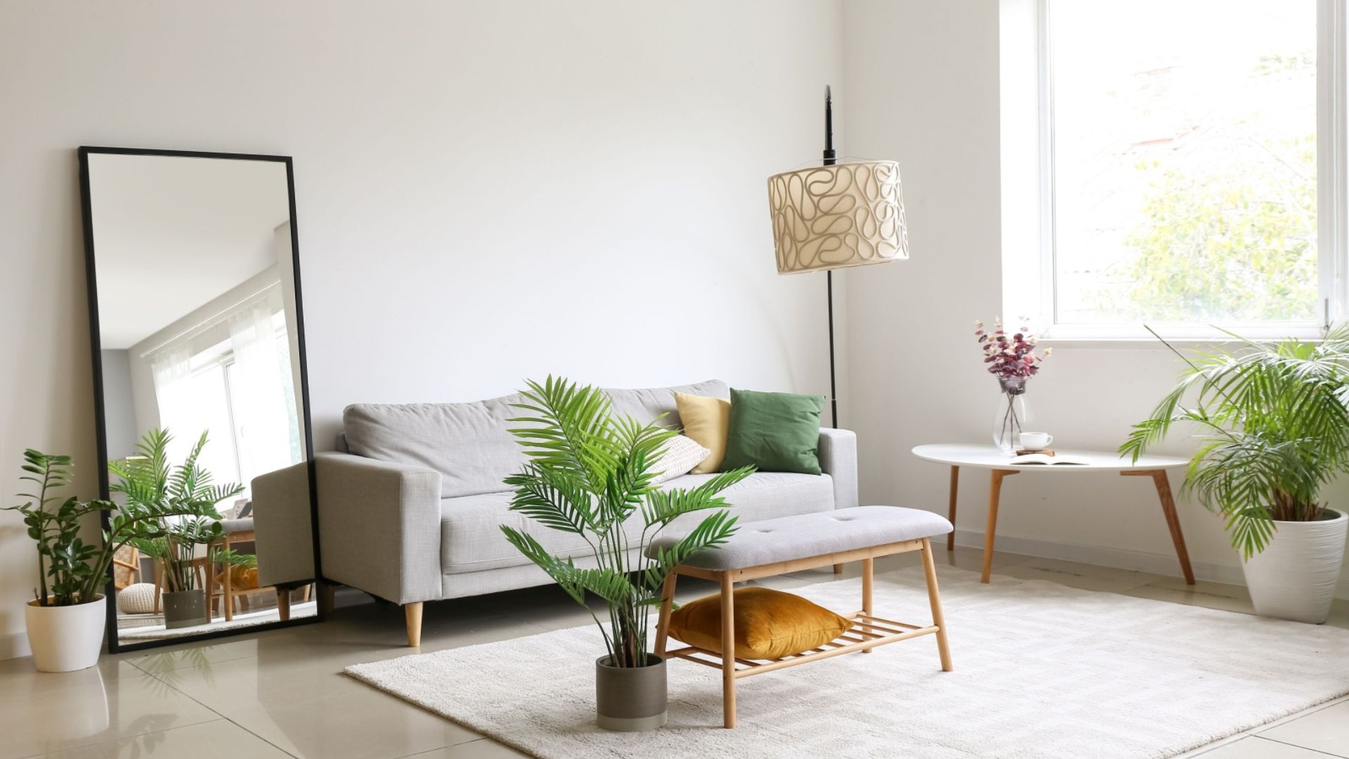 living room with a tall mirror, gray couch, white table and a big window