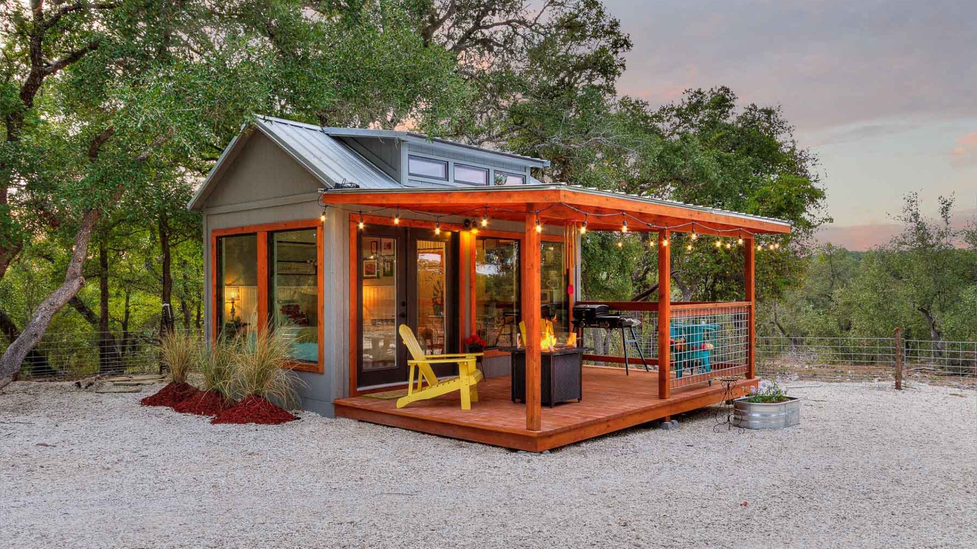 exterior of a tiny home with a patio with yellow chairs and string lights