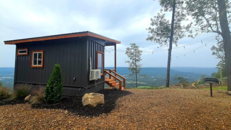Tiny container house located on a cliff edge, painted in black, with a charming porch