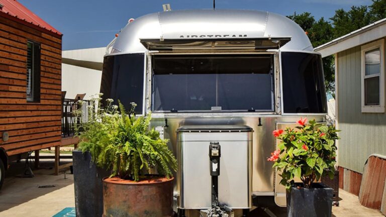 exterior of the shiny Airstream house with plants around it