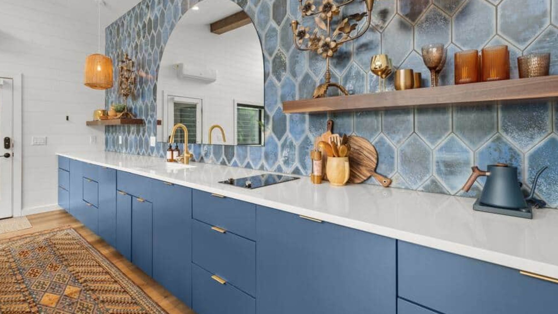 beautiful blue kitchen with blue counters and white countertops, floating shelves with trinkets,a big semi circle mirror, blue hexagonal tiles as backsplash wall