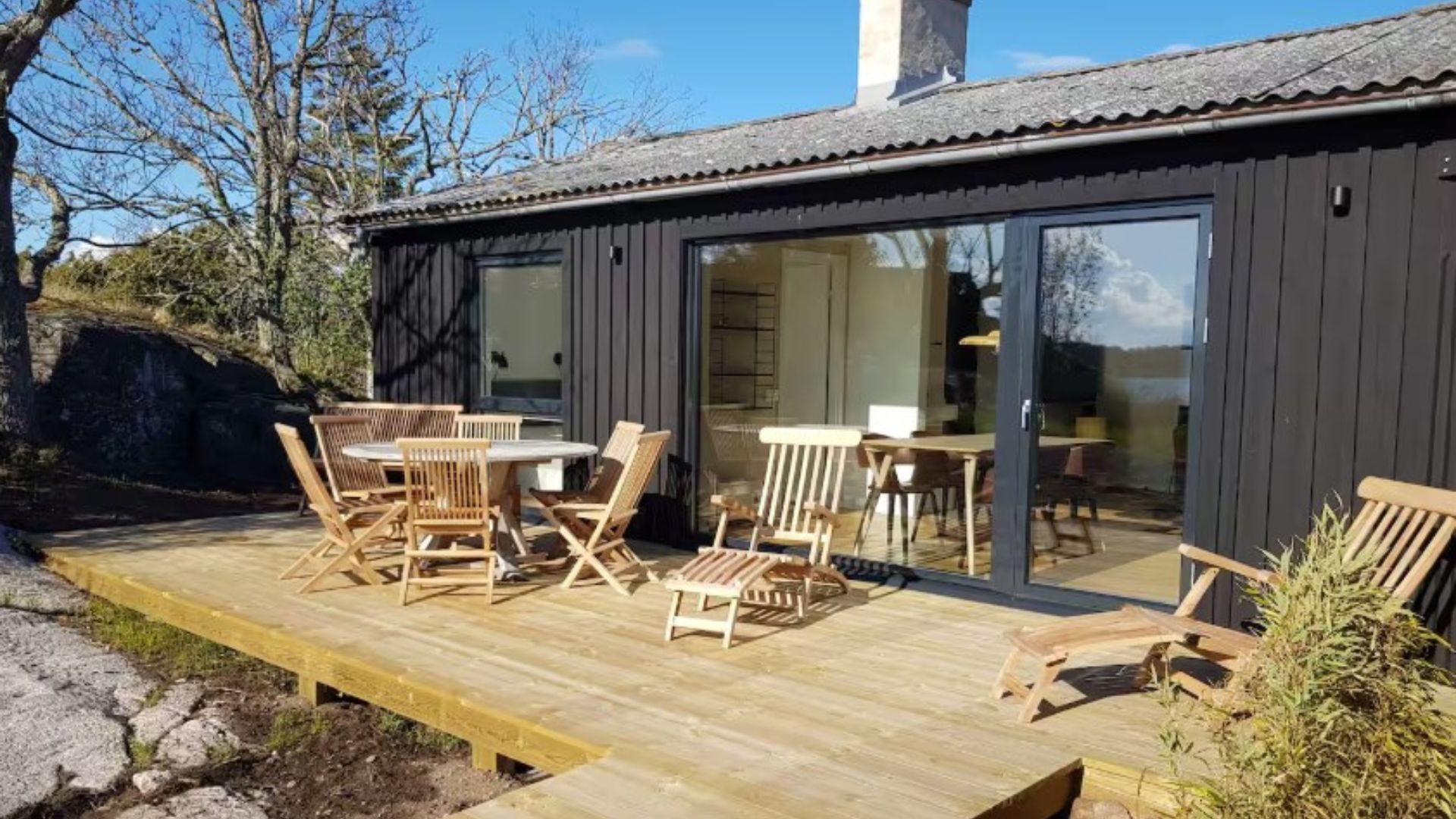 exterior of a container home with black walls and a wooden patio with wooden chairs and a table