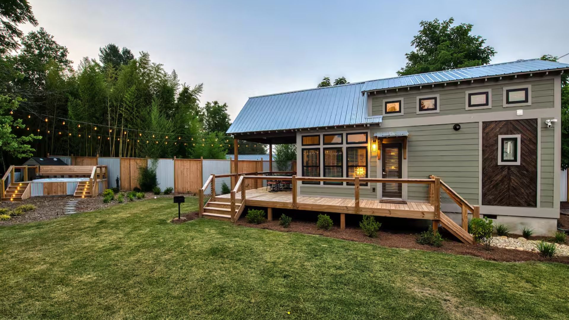 tiny house exterior done in light green, with a small porch, surrounded by green grass and trees