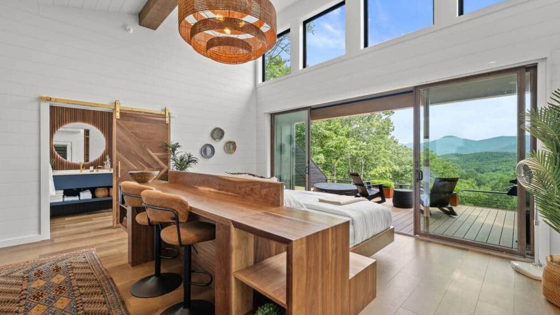 beautiful open concept bedroom withh a big window wall up front, a cozy bed, and some dining table and chairs behind the bed