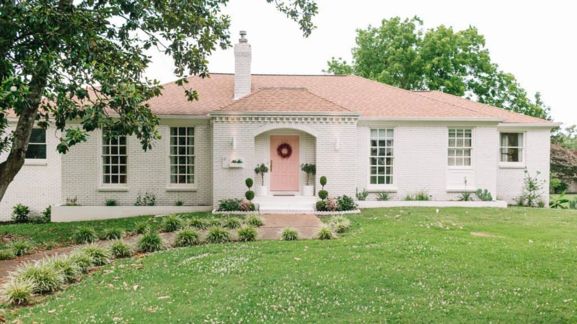 exterior of a home with white exterior, light pink doors and tiny bushes in front