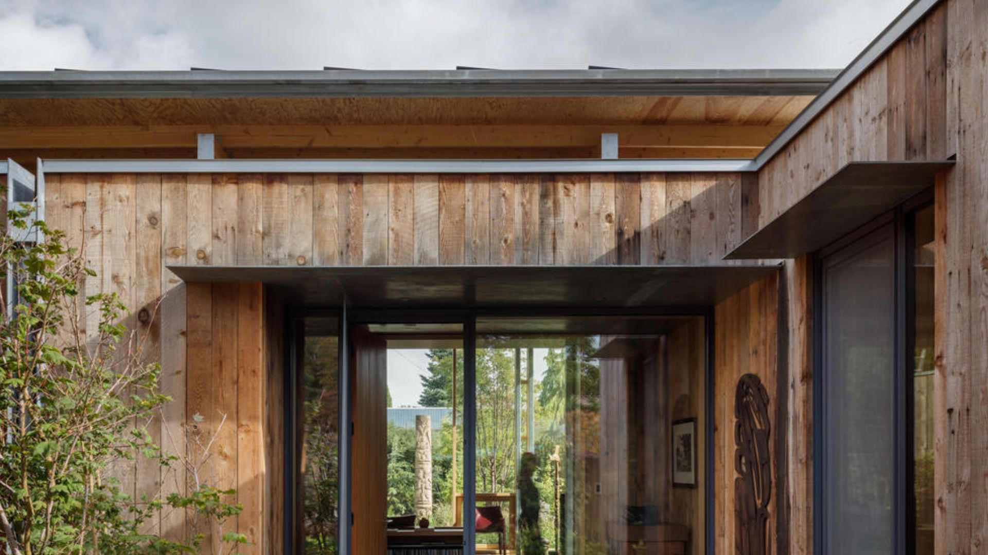 exterior of modern cabin house with flat roof and flack fenestration, lots of glass walls, and greenery around the cabin